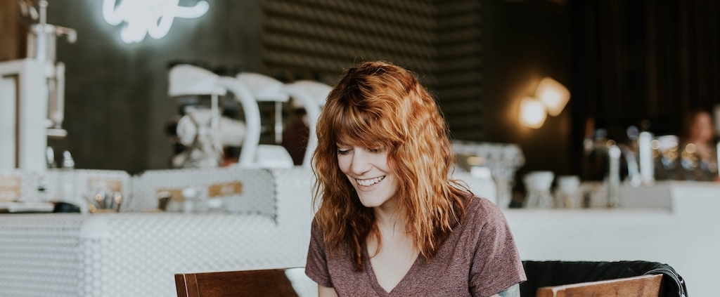 young-professional-female-smiling-at-computer-screen-in-cafe