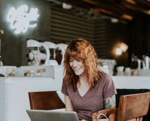 young-professional-female-smiling-at-computer-screen-in-cafe