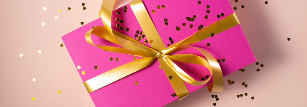 A pink gift card sized package wrapped with a gold bow