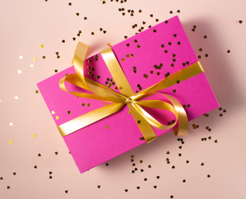 A pink gift card sized package wrapped with a gold bow