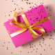 A pink gift card sized package wrapped with a gold bow