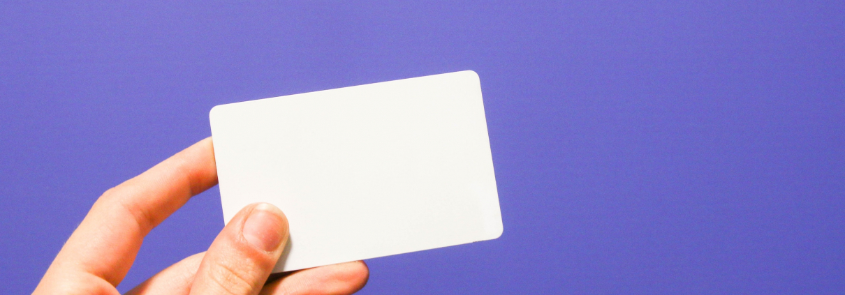 A hand holding a white card against a purple background.
