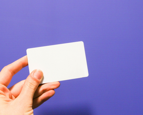 A hand holding a white card against a purple background.