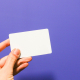 A hand holding a white card against a purple background.