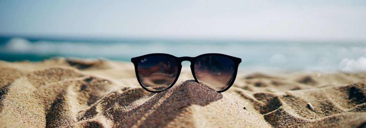 A pair of sunglasses resting on top of a sandhill on a sunny beach.