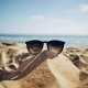 A pair of sunglasses resting on top of a sandhill on a sunny beach.